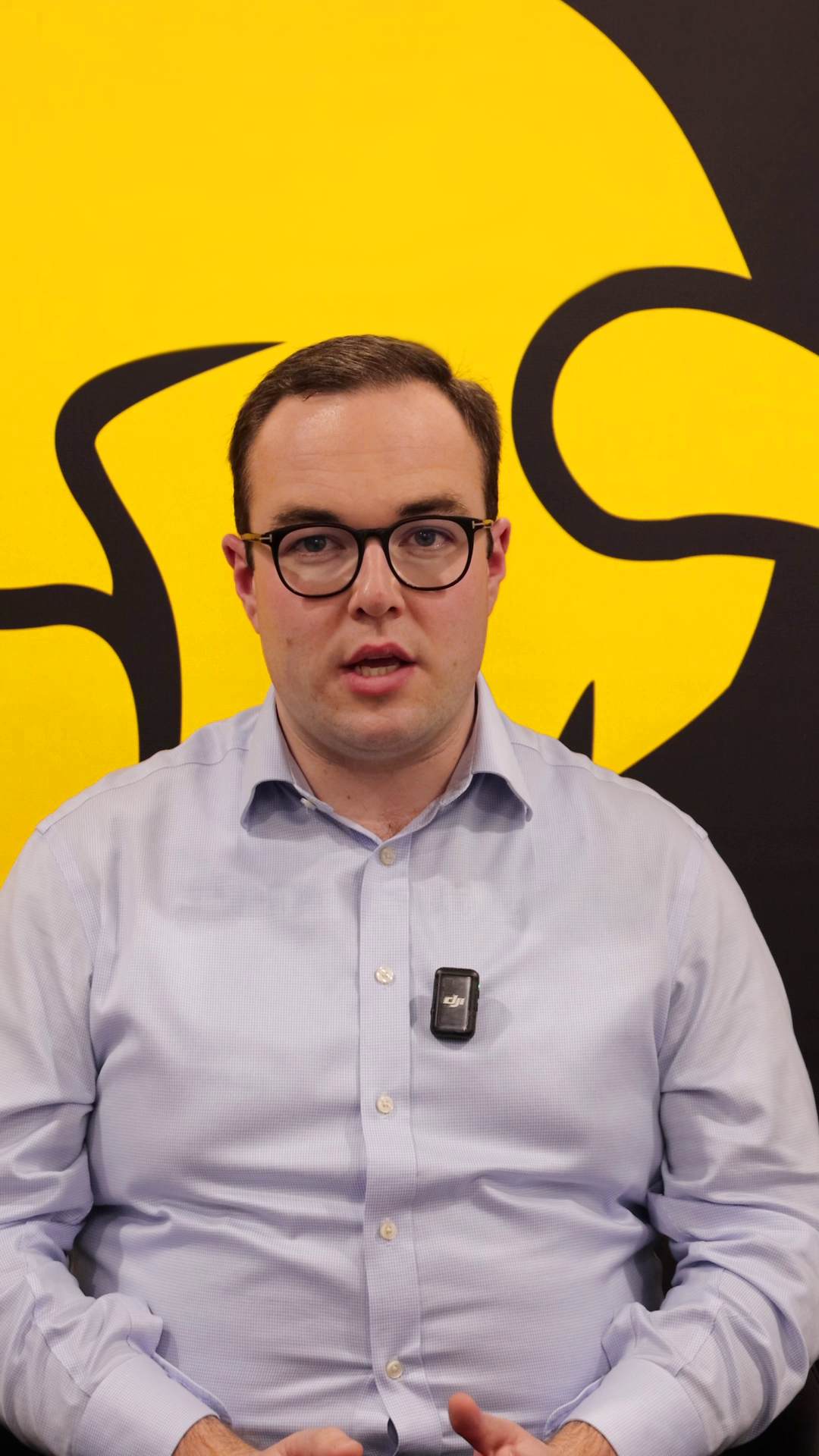 Video still: Jake speaking in front of a yellow and black branded background.