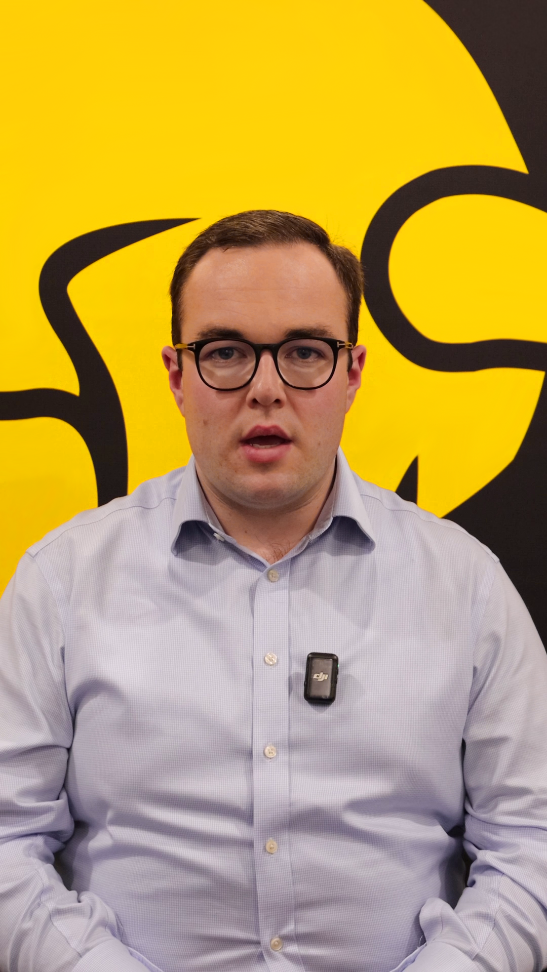 Video still: Jake speaking in front of a yellow and black branded background.
