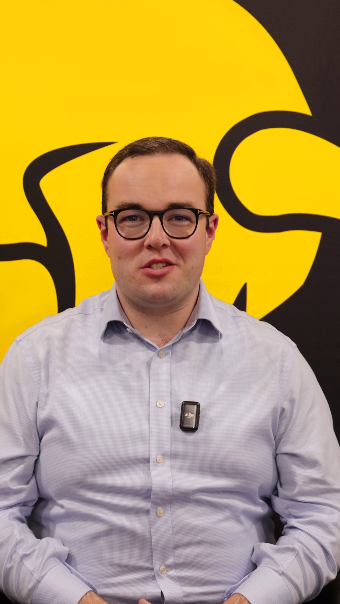 Video still: Jake speaking in front of a yellow and black branded background.