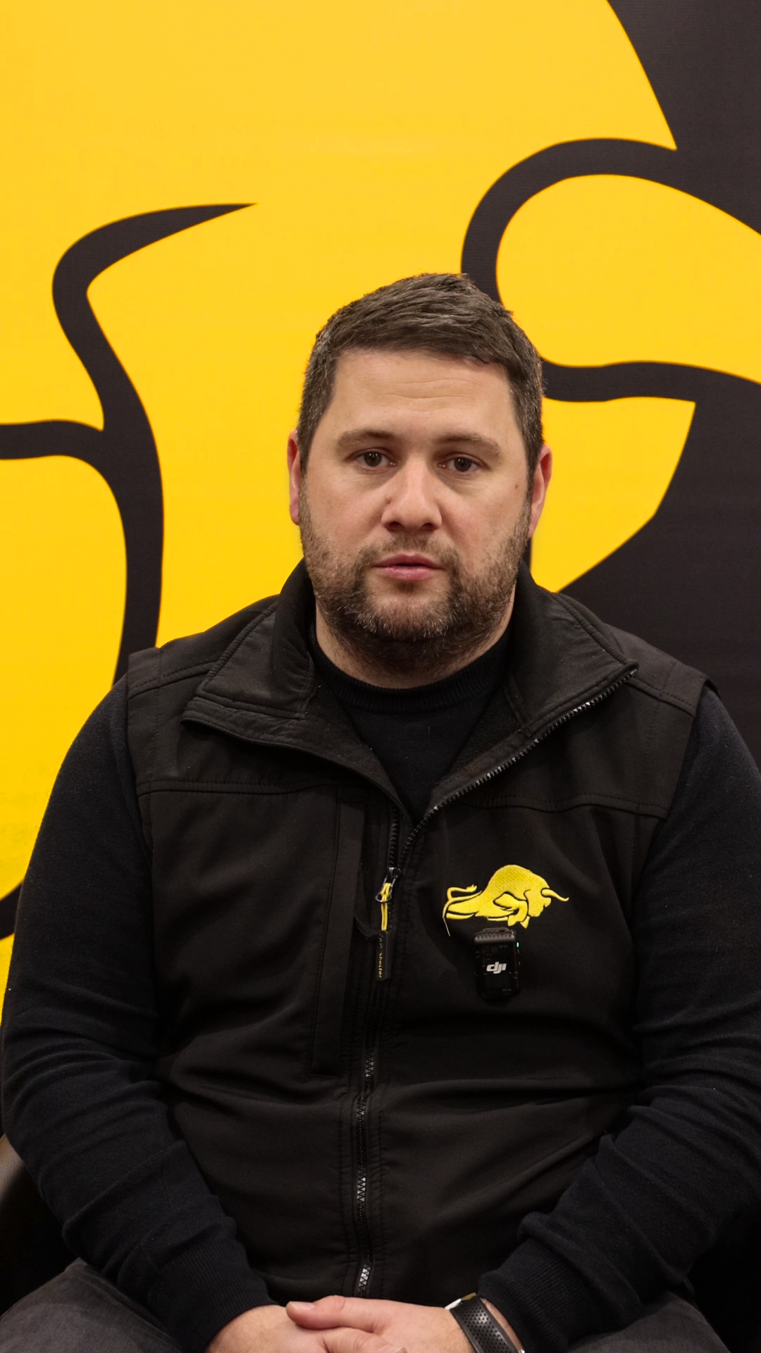 Video still: Liam speaking in front of a yellow and black branded background.