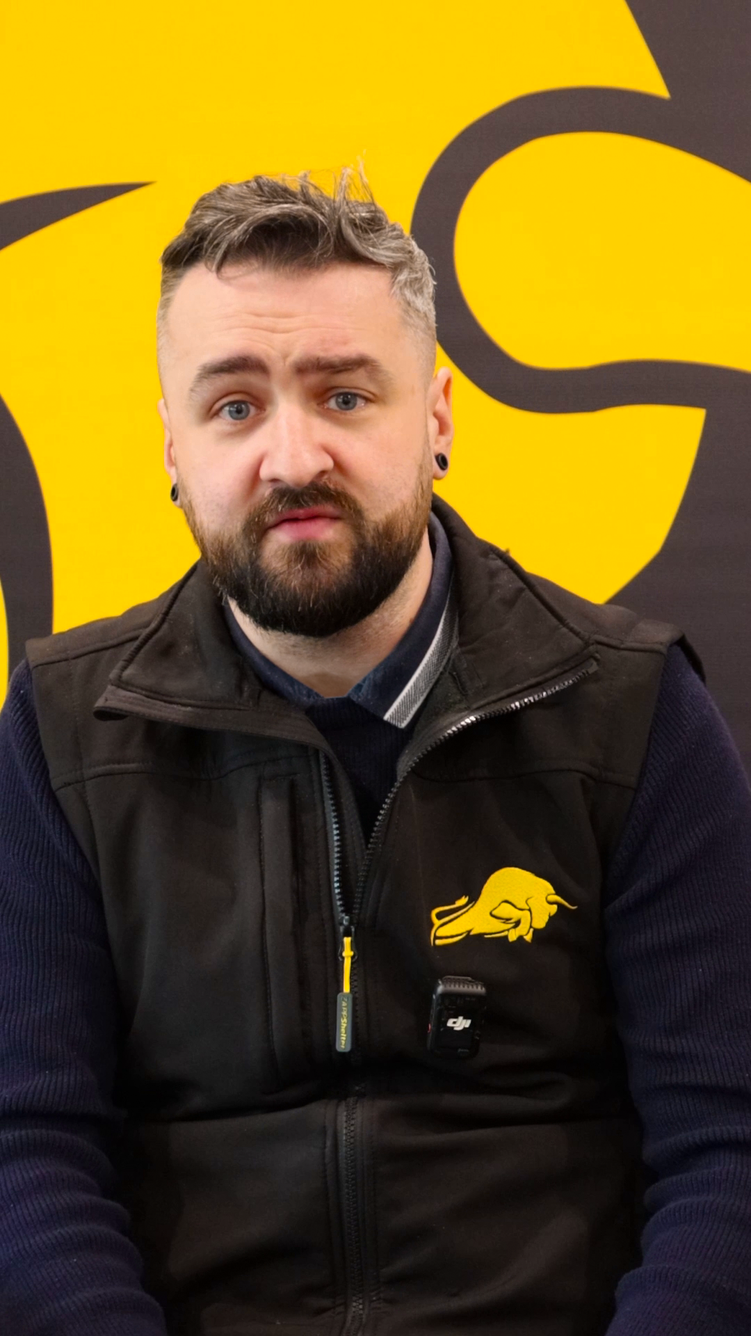 Video still: Peter speaking in front of a yellow and black branded background.