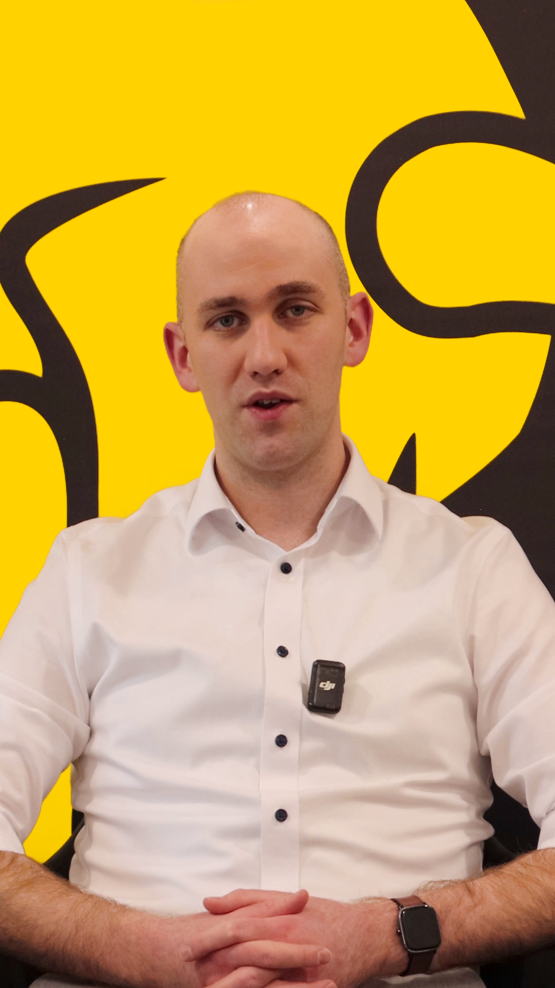 Video still: Stephen speaking in front of a yellow and black branded background.