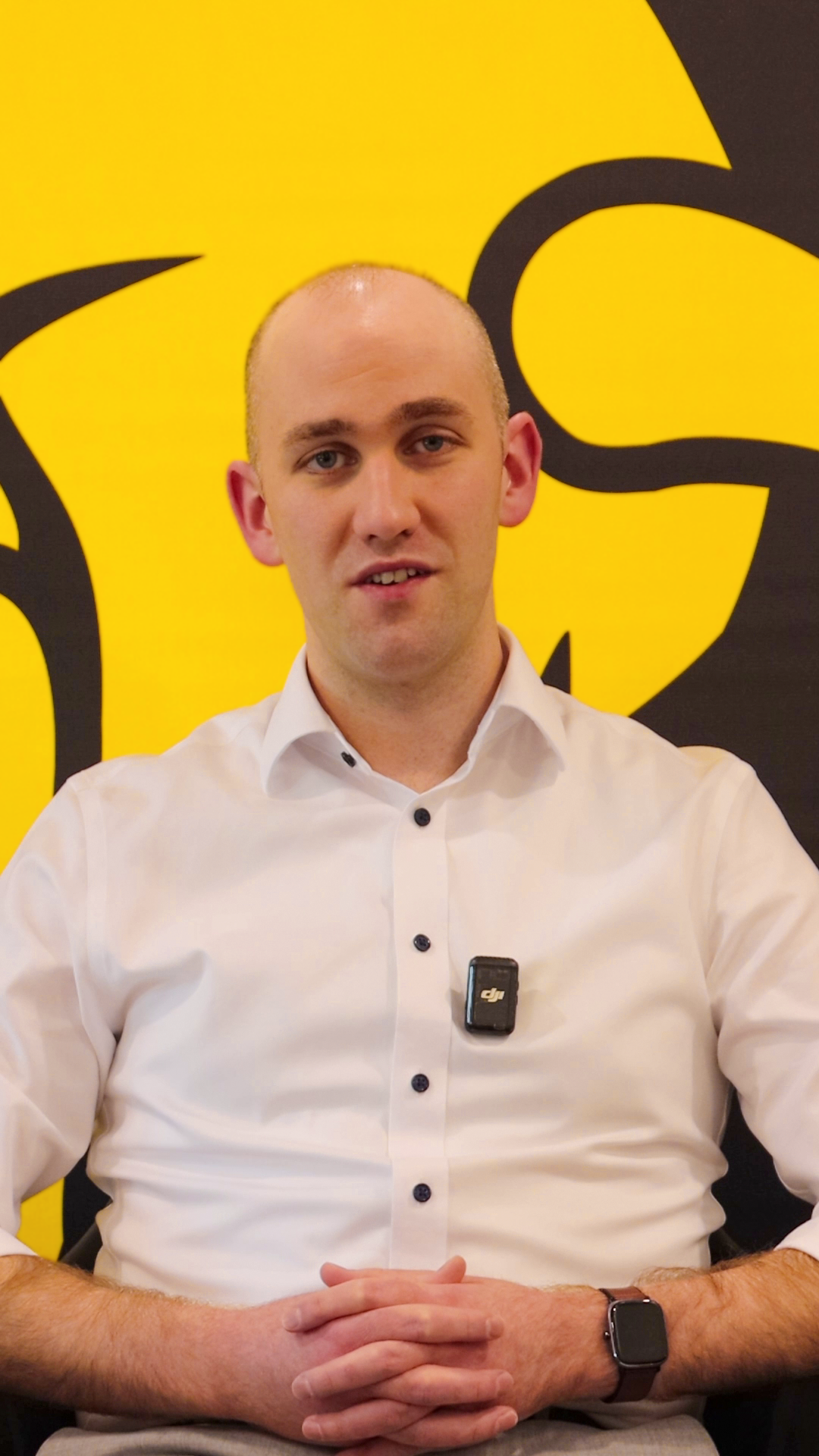 Video still: Stephen speaking in front of a yellow and black branded background.